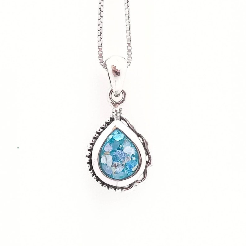 May include: A silver pendant necklace featuring a teardrop-shaped pendant. The pendant has a light blue and white speckled design, encased in a silver frame with a beaded edge. The necklace chain is a delicate silver box chain.