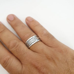 May include: A silver ring with Hebrew text inscribed on it. The ring is worn on a person's finger.