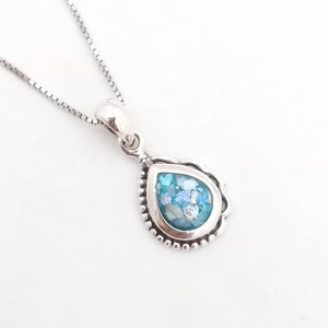 May include: A silver necklace featuring a teardrop-shaped pendant. The pendant has a light blue and white mosaic design set within a beaded silver frame. The chain is a delicate box chain style.