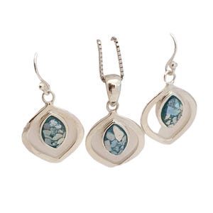 May include: A silver jewelry set featuring a pendant necklace and matching earrings. Each piece has a teardrop-shaped frame with a light blue, textured center. The earrings have a hook closure.