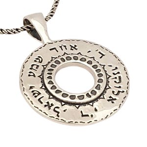 May include: A circular silver pendant on a twisted chain featuring Hebrew text engraved along the outer edge and a decorative border of small indentations surrounding the central circular cutout, creating a polished metallic finish.