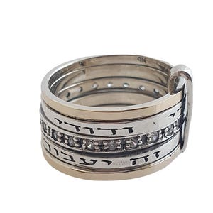 Puede incluir: Un anillo de plata con una banda de oro y una fila de piedras transparentes. El anillo tiene escritura hebrea.
