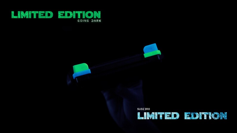 May include: A black gaming controller featuring bright neon green and blue accents on the shoulder buttons. The text LIMITED EDITION GOING DARK appears in green at the top, and SUBZERO LIMITED EDITION is printed in blue at the bottom right.