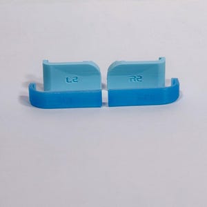 Puede incluir: Dos extensiones de gatillo para mando en color azul claro con acabado liso. La pieza izquierda tiene grabado el texto L2 y la derecha el texto R2. Estos componentes presentan un dise&ntilde;o curvo con una secci&oacute;n base en color azul oscuro.