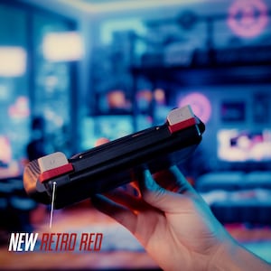 Puede incluir: Un mando de juego port&aacute;til negro con botones superiores blancos y detalles en rojo. Una fina l&iacute;nea blanca se&ntilde;ala desde el detalle rojo hacia el texto NEW RETRO RED impreso en blanco y rojo en la parte inferior izquierda.