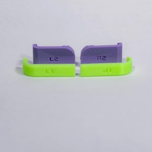 Puede incluir: Un juego de cuatro botones de hombro de repuesto para mando. Dos son de color verde ne&oacute;n brillante con etiquetas L1 y R1, y dos son de color morado claro con etiquetas L2 y R2. Estos peque&ntilde;os componentes de pl&aacute;stico sirven para personalizar mandos.