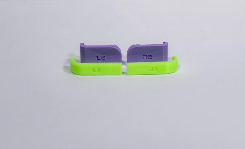 Puede incluir: Un juego de cuatro botones de hombro de repuesto para mando. Dos son de color verde ne&oacute;n brillante con etiquetas L1 y R1, y dos son de color morado claro con etiquetas L2 y R2. Estos peque&ntilde;os componentes de pl&aacute;stico sirven para personalizar mandos.