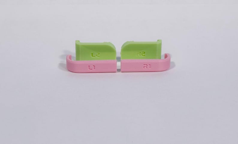 Puede incluir: Un conjunto de cuatro botones de gatillo de repuesto para mando. Dos botones son de color verde claro con marcas L2 y R2, y dos botones son de color rosa claro con marcas L1 y R1. Estos componentes de pl&aacute;stico tienen un acabado liso y uniforme.