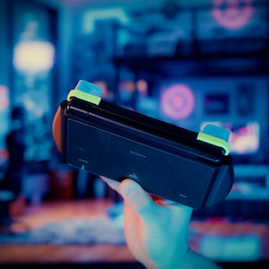 Puede incluir: Una consola de juegos port&aacute;til negra con un cuerpo rectangular que presenta el logotipo de Sony, agarres laterales integrados y botones superiores de color azul claro y verde lima situados en el borde superior del dispositivo.