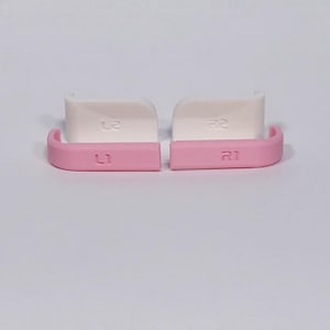 Puede incluir: Un conjunto de cuatro botones de repuesto para mando, que incluye dos gatillos blancos L2 y R2 y dos botones superiores rosas L1 y R1. Cada bot&oacute;n est&aacute; claramente etiquetado con su funci&oacute;n, con un acabado liso y un dise&ntilde;o curvado.