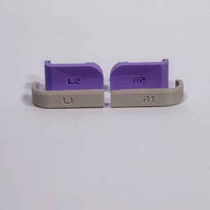 Puede incluir: Un juego de cuatro botones de hombro de repuesto para mando, compuesto por dos gatillos morados L2 y R2 y dos botones superiores beige L1 y R1. Cada pieza est&aacute; claramente grabada con su etiqueta correspondiente L1, R1, L2 y R2.