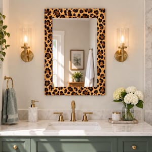 May include: A rectangular wall mirror featuring a bold leopard print frame with black, brown, and tan spots. The mirror has a clean, reflective glass surface and is mounted vertically, showcasing a classic rectangular shape with a wide, patterned border.