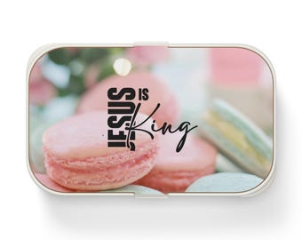 May include: A rectangular metal tin with rounded corners featuring a printed image of pastel-colored macarons. The text "JESUS IS King" is printed in black lettering across the center of the lid, overlaying the soft pink and blue macaron design.