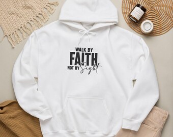 May include: A white hooded sweatshirt featuring the black printed text WALK BY FAITH NOT BY SIGHT on the chest. The garment includes a front kangaroo pocket, long sleeves with ribbed cuffs, and a matching white drawstring cord at the neckline.