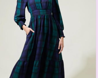 Puede incluir: Un vestido midi con estampado de cuadros en azul oscuro y verde, cuello alto con volantes, mangas largas con puños fruncidos, cintura entallada y falda escalonada con bolsillos laterales. La prenda presenta un cuerpo estructurado.
