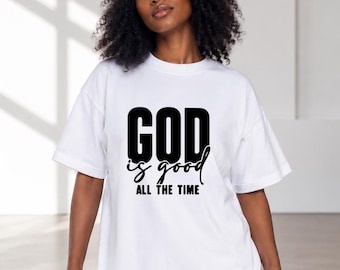 May include: A white short-sleeved t-shirt featuring the black printed text GOD is good ALL THE TIME on the chest, paired with a matching white baseball cap. The shirt has a crew neckline and a relaxed fit, showcasing bold typography.