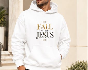 Puede incluir: Una sudadera con capucha blanca que presenta el texto FALL WITH JESUS en letras doradas y negras en el pecho, acompañado de pequeños iconos de copos de nieve. La sudadera incluye un bolsillo tipo canguro, mangas largas y puños y dobladillo acanalados.