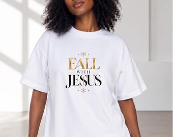 Puede incluir: Una camiseta blanca de manga corta con el texto en dorado y negro "FALL WITH JESUS" impreso en el pecho. El diseño incluye pequeños detalles dorados en forma de estrella encima y debajo del texto, con una cruz integrada en la letra U de Jesus.