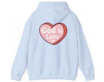 Puede incluir: Una sudadera con capucha de color azul claro que presenta un gráfico de un corazón rosa grande en la espalda. El corazón tiene un borde rojo oscuro y contiene el texto blanco "God is Love" en una fuente negrita y redondeada con estrellas.