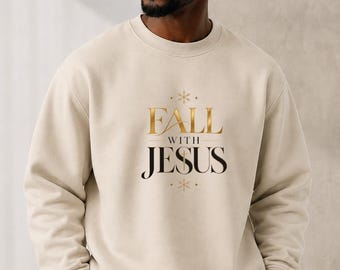 Puede incluir: Una sudadera beige de cuello redondo con el texto FALL WITH JESUS en letras doradas y negras, acentuado por pequeños símbolos de estrellas encima y debajo de las palabras. La sudadera tiene mangas largas con puños y cuello acanalados.