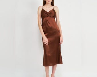 Puede incluir: Un vestido tipo lencero de largo midi en color marrón chocolate sólido. La prenda presenta un diseño sin mangas con tirantes finos, un escote en V con un detalle de nudo central en el busto y un acabado satinado que cae de forma recta.