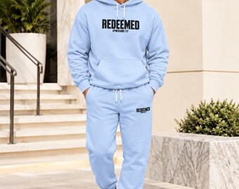 Puede incluir: Un conjunto a juego de color azul claro que consta de una sudadera con capucha, pantalones de chándal y una gorra de béisbol. La sudadera y el pantalón llevan el texto negro "REDEEMED" y "EPHESIANS 1:7". La gorra muestra la palabra "REDEEMED".