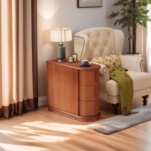 May include: A wooden side table with three drawers and a ribbed front. A green lamp with a cream shade sits on top, along with a cup and framed photos. A beige armchair and green throw blanket are in the background.
