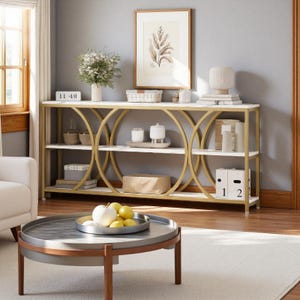 May include: A white and gold console table with three shelves and a marble top. The table has a gold circular design on the sides. The shelves are filled with decorative items, including books, boxes, and candles. A round coffee table with a tray of fruit sits in front.