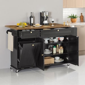 Op de afbeelding: Een zwart keukeneiland met een houten werkblad. Het heeft een ingebouwde vuilnisbak, lades en kastruimte. Op het werkblad staan een koffiezetapparaat, een fles wijn en een fruitschaal. Aan de zijkant zit een handdoekenrek.