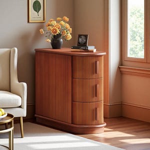 Puede incluir: Un mueble de madera de estilo moderno de mediados de siglo, con tres cajones y un diseño curvo. El mueble es de color marrón rojizo cálido y tiene detalles verticales acanalados. Encima hay un jarrón con flores amarillas.