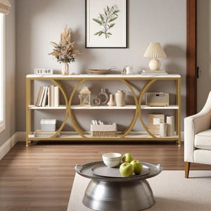 May include: A modern console table with a white marble top and gold metal frame. The table features three shelves and a unique circular design. Decorative items like books, vases, and a lamp are displayed on the table. A round coffee table with a metal tray and green apples is in front.