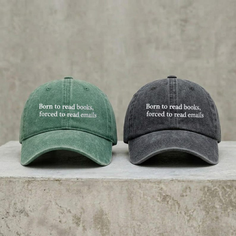 May include: Two baseball caps, one in a washed green and one in a washed charcoal gray, both featuring the white embroidered text Born to read books, forced to read emails on the front panel. Each cap has a curved brim and a six-panel construction.