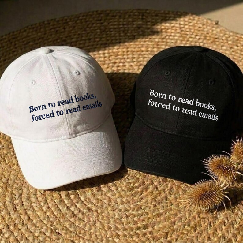 May include: A white baseball cap with dark blue text and a black baseball cap with white text. Both caps feature the embroidered phrase: Born to read books, forced to read emails. Each cap has a structured crown, a curved brim, and eyelets.