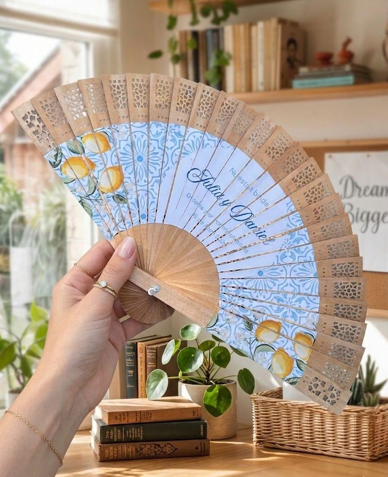 Puede incluir: Abanico de mano de madera con un dise&ntilde;o estampado en azul claro y blanco con limones. El abanico tiene un dise&ntilde;o calado decorativo a lo largo del borde superior y el texto "Julia y Daniel".