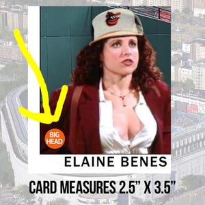 May include: A trading card featuring a photo of Elaine Benes from the TV show Seinfeld. She is wearing a red jacket, a white shirt, and a baseball cap with the Baltimore Orioles logo. The card measures 2.5 inches by 3.5 inches. The text "Elaine Benes" and "Card Measures 2.5" x 3.5" are printed on the card.