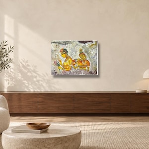 Puede incluir: Una impresión de arte mural rectangular que presenta una pintura texturizada de estilo desgastado de dos figuras con vestimenta amarilla y naranja. Las figuras están adornadas con joyas y tocados tradicionales, y una de ellas sostiene una flor de loto rosa sobre un fondo moteado.