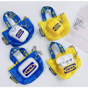 Pode incluir: Quatro capas de AirPod inovadoras no estilo de sacolas de compras IKEA. Duas são azuis, duas amarelas, com alças azuis e o logotipo da IKEA. Uma capa está aberta, revelando fones de ouvido brancos.