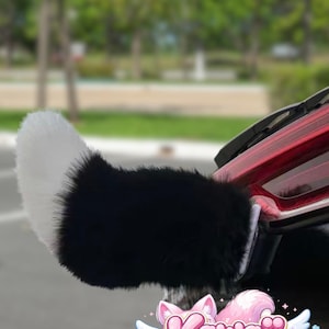 May include: A fluffy black and white tail attachment, possibly for a vehicle, with a white tip and a black base. The tail is attached to a car. The image includes the "Kawaii Morph" logo.