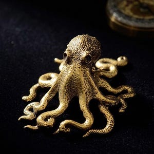 May include: A detailed, golden-colored octopus figurine with textured skin and multiple tentacles. The sculpture is set against a dark background, highlighting its intricate design. A compass is visible in the background.