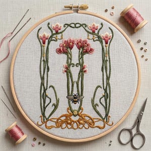 May include: An Art Nouveau style embroidery hoop featuring a floral design with pink and green accents, and a bee. The embroidery is set in a wooden hoop, with needles, thread spools, and scissors nearby.