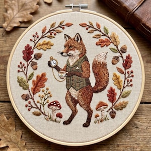 May include: Embroidered artwork featuring a fox dressed in a tweed vest, holding a pocket watch and teacup. The fox is surrounded by autumn leaves, acorns, and mushrooms, all within a wooden embroidery hoop. The color palette includes shades of brown, orange, and green.