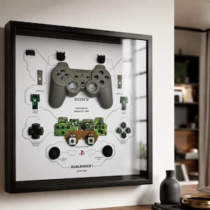 Könnte beinhalten: Gerahmtes Kunstwerk mit einem zerlegten PlayStation DualShock 1 Controller. Der graue Controller und seine Komponenten sind auf weißem Hintergrund mit schwarzem Rahmen dargestellt. Der Text "SONY" und "Launched on August 27, 1997" sind sichtbar.