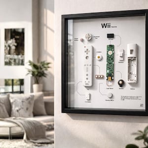 Könnte beinhalten: Gerahmte Darstellung einer zerlegten Wii-Fernbedienung, die ihre inneren Komponenten zeigt. Die weiße Fernbedienung befindet sich neben ihren Teilen, einschließlich der Hauptplatine, des Lautsprechers und der Tasten. Der Rahmen ist schwarz, der Hintergrund ist weiß.