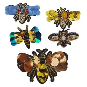 May include: Five decorative insect brooches. The brooches feature intricate designs with sequins, beads, and embroidery. The insects include bees and a dragonfly, with a variety of colors including gold, black, blue, and iridescent green.