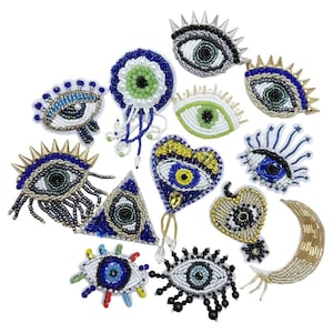 Può includere: Una collezione di abbellimenti a forma di occhio con perline in vari design. Gli occhi presentano perline blu, verdi e dorate, alcuni incorporando punte, cuori e forme di luna crescente. Questi pezzi decorativi sono probabilmente per l'artigianato o la moda.