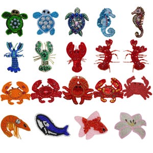 May include: A selection of beaded sea creature pins, featuring turtles, seahorses, crabs, lobsters, and fish. The pins are in various colours such as green, blue, red, and orange, with detailed beadwork. These decorative pins are ideal for adding a nautical theme to clothing or accessories.