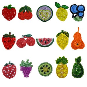 Op de afbeelding: Een verzameling van met kralen versierde fruitvormige versieringen. De collectie omvat een rode aardbei, kersen, een watermeloen schijf, een citroen, een peer, een kiwi, een ananas en een tros druiven. Elk stuk is gemaakt met kleurrijke kralen.