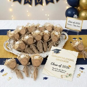 Può includere: Bomboniere di laurea, ognuna un piccolo bouquet di fiori secchi avvolti nella juta. Un cartello recita "Classe 2026 Favors - Take One!" e una carta dice "Congratulazioni, Laureato! Classe 2026. Grazie per aver condiviso questa speciale pietra miliare."