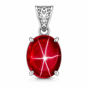 May include: A silver pendant featuring an oval-shaped, deep red star gemstone held by four prongs. The top of the pendant has an ornate, filigree-style silver bail with intricate cut-out patterns, providing a decorative attachment point.