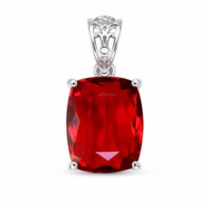 May include: A cushion-cut, deep red gemstone pendant set in a silver-toned metal prong setting. The pendant features a decorative, openwork filigree bail at the top, providing a detailed contrast to the smooth, faceted surface of the vibrant red stone.